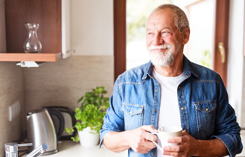 Happy senior man in the kitchen. An old man inside the house, holding a cup of coffee.