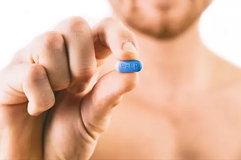 Close-up of a hand pinching a blue PrEP-labelled pill — Pre-Exposure Prophylaxis medication used to prevent HIV infection.