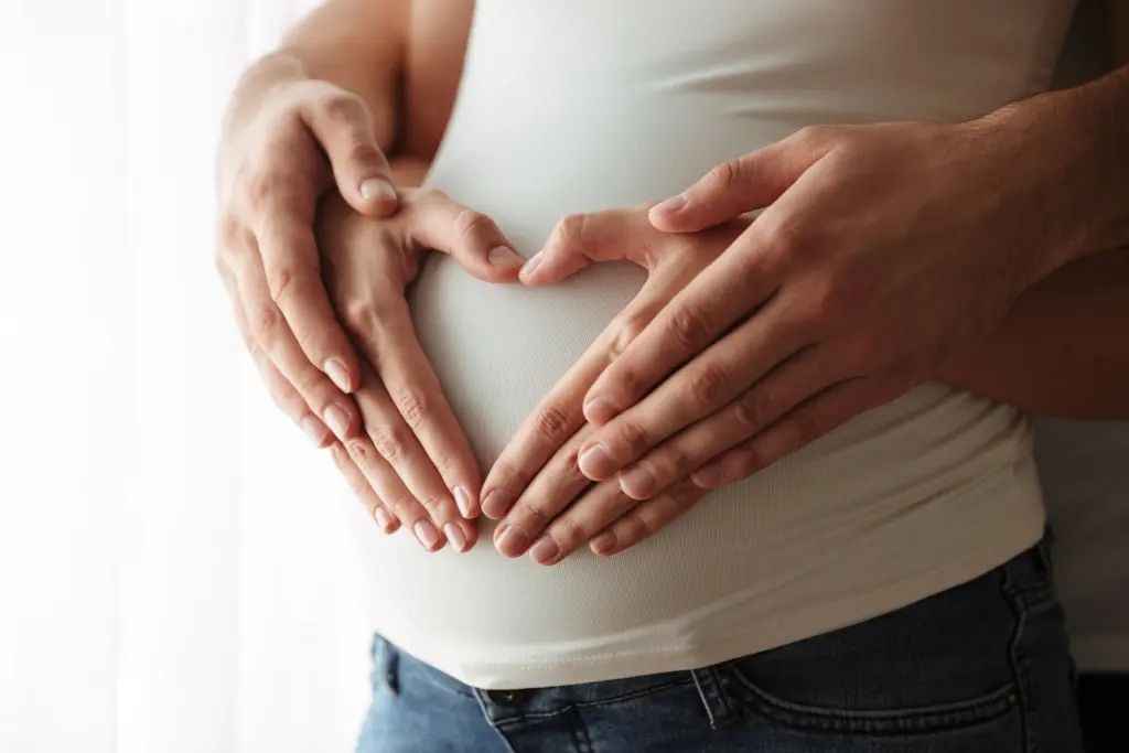 Close-up of a couple's hands resting on a pregnant woman's belly showing relevance to vaccines during pregnancy decisions.